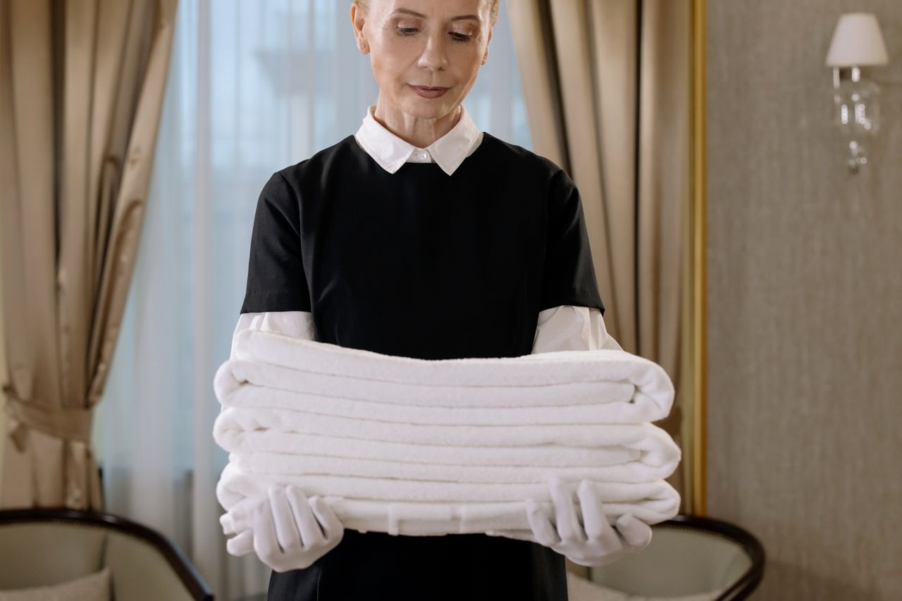 Skilled housekeeper carrying a pile of clean towels in an upscale hotel room, highlighting refinement and attentive service.